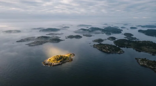 Vue aérienne symbolique d'un phare éclairant une petite île isolée au milieu d'un vaste archipel, représentant l'identification d'une niche médiatique à fort potentiel